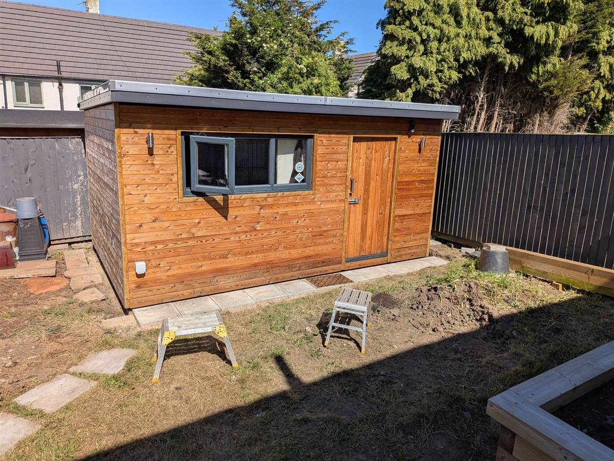 Finished building in sunshine — oiled cedar cladding, anthracite-framed windows and door, grey EPDM flat roof